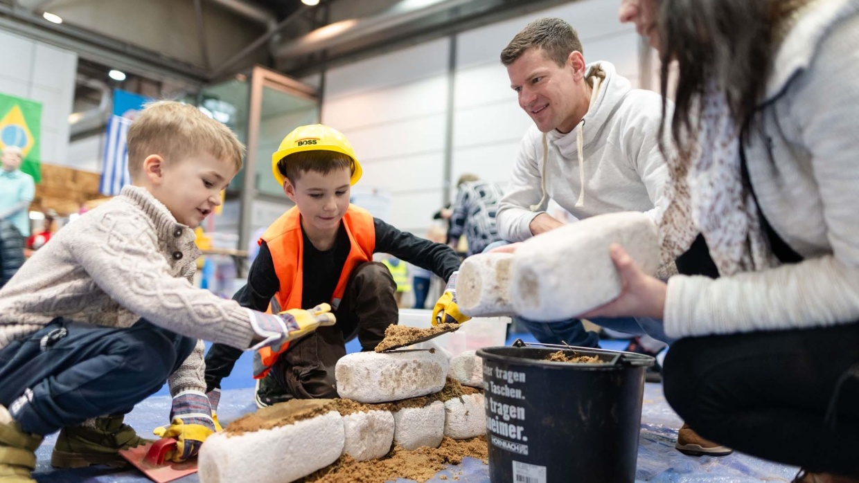 Mit viel Freude baut eine Familie auf der Kinderbaustelle der HANDWERK live mit Steinen und Sand.