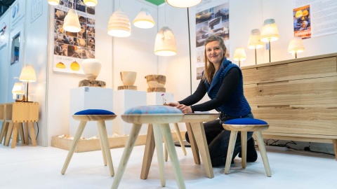 Eine Ausstellerin präsentiert freudestrahlend auf HANDWERK live ihre kunstvoll gefertigten Hocker und Lampen.