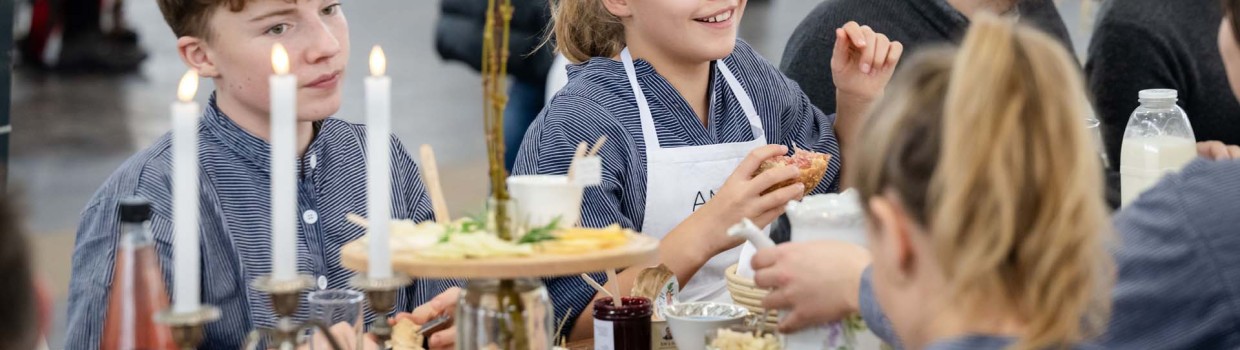 Several visitors are sitting together at a laid table at the HAUS-GARTEN-FREIZEIT trade fair, chatting, while a boy and a girl can also be seen at the table.