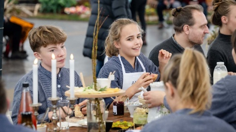 An einem gedeckten Tisch auf der HAUS-GARTEN-FREIZEIT sitzen mehrere Besuchende im Gespräch beisammen, während auch ein Junge und ein Mädchen mit am Tisch zu sehen sind.