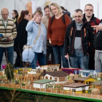 Many interested visitors at the HAUS-GARTEN-FREIZEIT trade fair are intently examining a detailed miniature model featuring various houses and lovingly designed gardens.