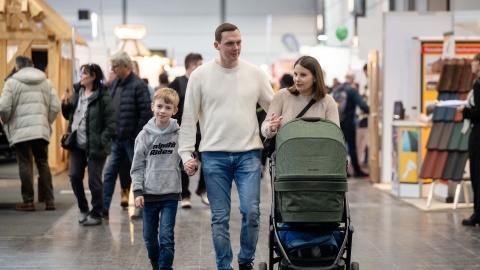 Zu sehen ist eine Familie (Eltern, ein kleiner Sohn und ein Kinderwagen), die über die HAUS-GARTEN-FREIZEIT geht.