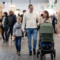 The image shows a family (parents, a young son and a pram) walking across HAUS-GARTEN-FREIZEIT.