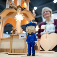 In the foreground, you can see the carved Leipzig trade fair mascot, and in the background, slightly faded, you can see other wooden figures and the exhibitor at HANDWERK live.