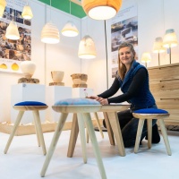 An exhibitor beams with joy as she presents her artistically crafted stools and lamps at HANDWERK live.