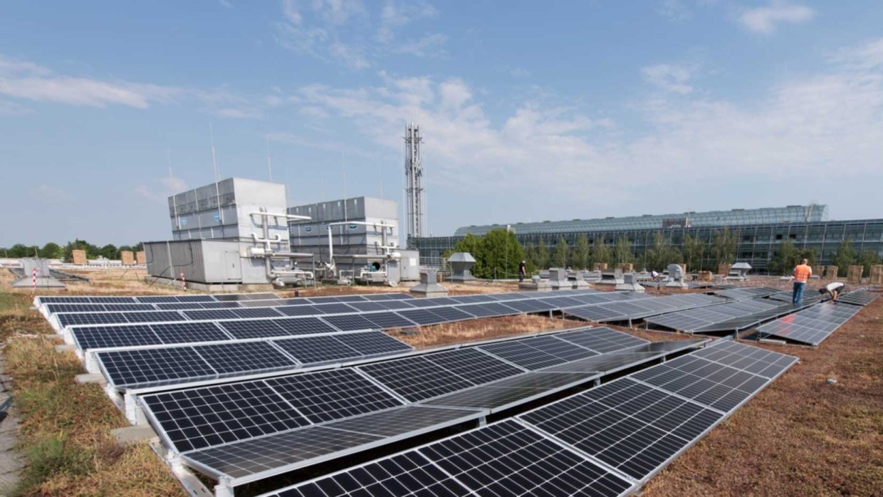 Solaranlage auf einem Flachdach mit technischen Anlagen und zwei arbeitenden Personen im Hintergrund.