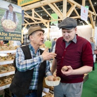 2 men are talking at a booth selling potatoes. 2 men are talking at a booth selling potatoes.