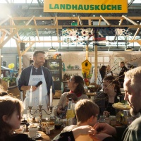 Eine Gruppe an Personen isst Frühstück bei dem Stand der Landhausküche.