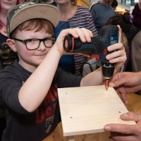 Ein Junge hält einen Akkuschrauber und dreht Schrauben in ein Holzbrett.